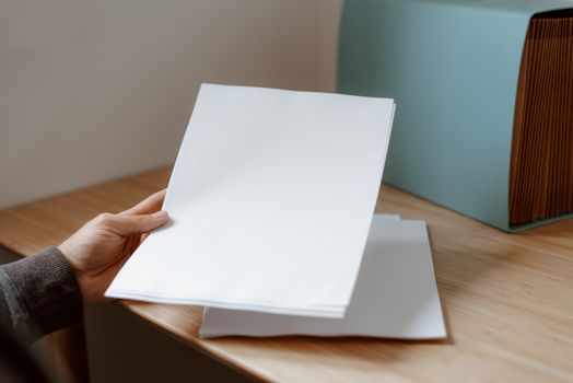 Home Crop anonymous person demonstrating empty sheet of paper against wooden table with folder for documents